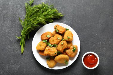 Lezzetli nugget tabağı, ketçap ve siyah masa üzerinde bitkiler.