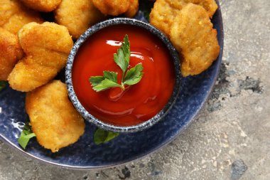 Lezzetli nugget tabağı, bir kase ketçap ve gri grunge masasında bitkiler, yakın plan.