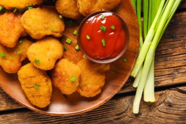 Lezzetli nugget tabağı, bir kase ketçap ve sebzeler ahşap masada, yakın plan.