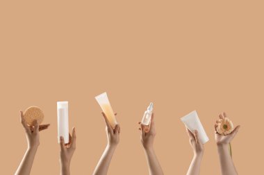 Bej arka planda kozmetik ürünleri ve çiçek tutan eller