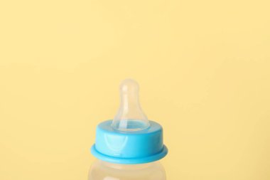 Soluk sarı arka planda bebek için süt şişesi