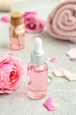 Gül özü ve beyaz masa üzerinde çiçekler olan kozmetik yağı şişeleri.