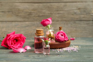 Gül özü ve ahşap masa üzerinde çiçekler olan kozmetik yağı şişeleri.