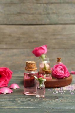 Gül özü ve ahşap masa üzerinde çiçekler olan kozmetik yağı şişeleri.
