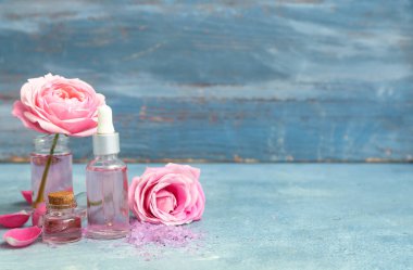 Mavi masa üzerinde gül özü ve çiçekler olan kozmetik yağları şişeleri.