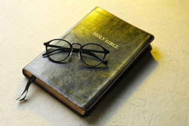 Gri arka planda gözlüklü kutsal İncil.