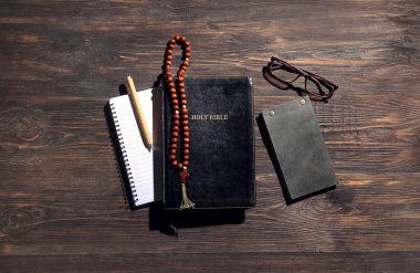 Kutsal İncil, defterler, dua boncukları, gözlük ve kalem tahta arka planda.