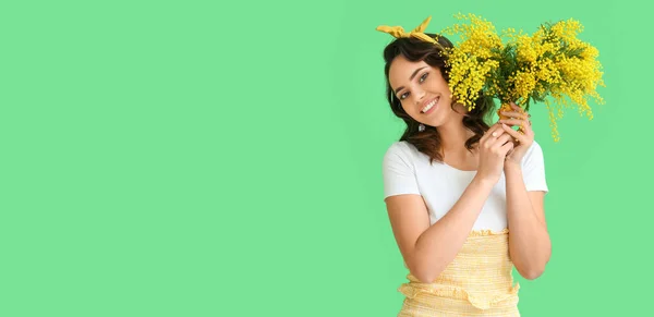 stock image Beautiful young woman with bouquet of mimosa flowers on green background with space for text