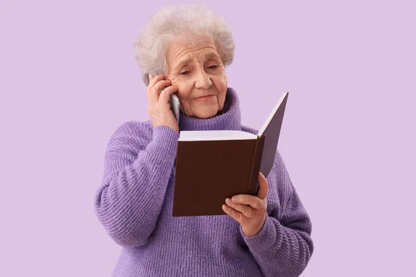 Mulher Sênior Com Livro Falando Por Telefone Celular Fundo Lilás — Fotografia de Stock