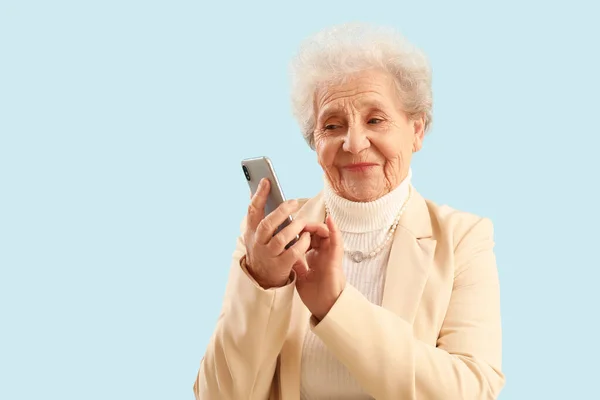 Starsza Kobieta Korzystająca Telefonu Komórkowego Niebieskim Tle — Zdjęcie stockowe