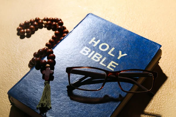 Holy Bible, prayer beads and eyeglasses on beige background