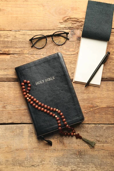 Holy Bible, prayer beads, notebook, pen and eyeglasses on wooden background