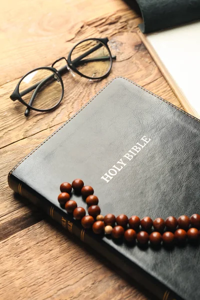 Holy Bible, prayer beads and eyeglasses on wooden background