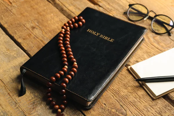 Holy Bible and prayer beads on wooden background