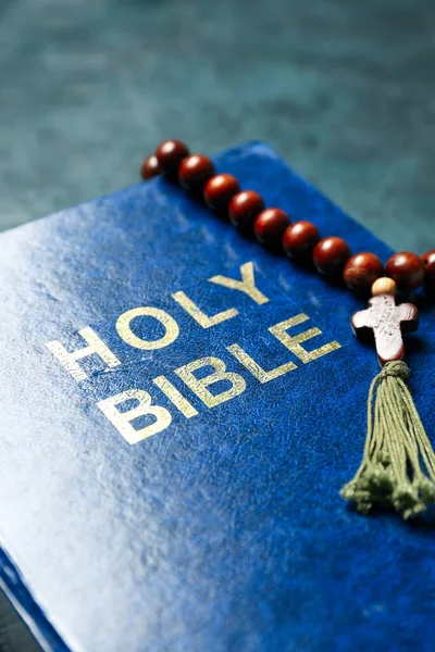 Holy Bible with prayer beads on dark background, closeup