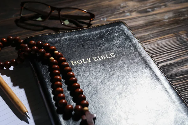 Holy Bible with prayer beads on wooden background, closeup