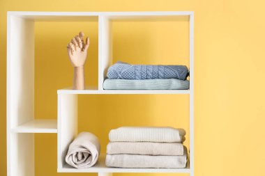 Güzel süveterleri ve bej duvarın yanında ahşap eli olan raf ünitesi.