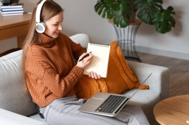 Not defteri olan kız öğrenci evdeki kanepede ders çalışıyor.