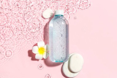 Bir şişe kaplıca taşlı mikiler suyu ve pembe zemin üzerinde suyla tesisat çiçeği.
