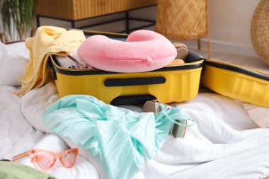 Yatakta plaj aksesuarlarıyla dolu bavulu aç.