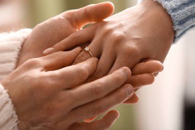 Erkek kadının parmağına nişan yüzüğü takıyor, yakın plan.