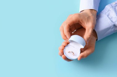 Mavi arka planda nişan yüzüğü olan bir adam.