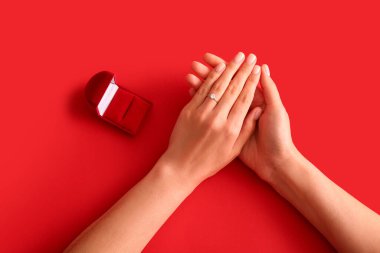 Kırmızı arka planda nişan yüzüğü olan kadın.