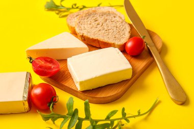 Sarı zemin üzerinde işlenmiş peynir, ekmek ve domates olan tahta