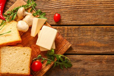 Kahverengi ahşap arka planda işlenmiş peynir, ekmek ve sebzeli tahta.