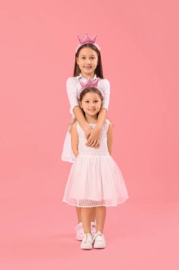 Taçlı küçük kızlar pembe arka planda sarılıyorlar. Çocuk Bayramı kutlaması