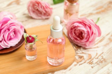 Gül özlü kozmetik yağı şişeleri ve açık ahşap masa üzerinde çiçekler.