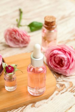 Gül özlü kozmetik yağı şişeleri ve açık ahşap masa üzerinde çiçekler.