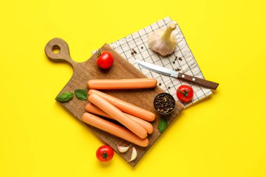 Board of tasty sausages with basil and tomatoes on yellow background clipart