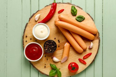 Yeşil ahşap arka planda fesleğenli ve biberli lezzetli sosisler.