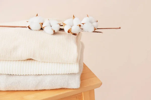 stock image Chair with beautiful sweaters and cotton branch near beige wall in room, closeup