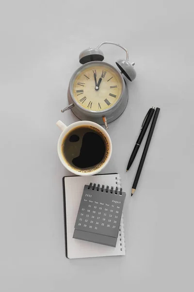 Flip paper calendar with alarm clock and cup of coffee on grey background