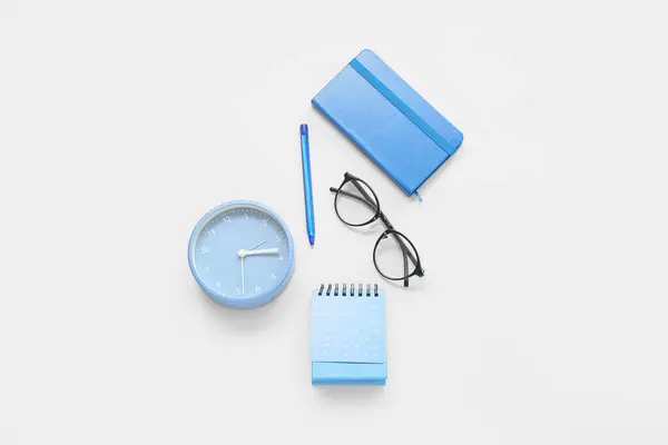 Flip paper calendar, alarm clock, eyeglasses and notebook on blue background