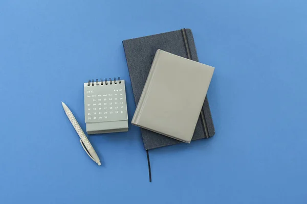 stock image Flip paper calendar for August with notebooks and pen on blue background