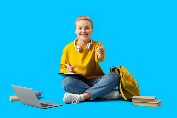 Female student with clipboard showing thumb-up on blue background