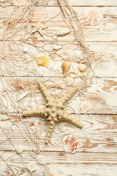 Beautiful starfish with seashells and net on light wooden background