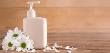 Bir şişe kozmetik ürünü ve ahşap zemin üzerinde papatya çiçekleri.