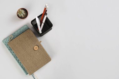 Kırtasiye tutucusu, not defterleri ve gri arka planda kaktüs.