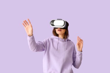 Pretty young woman in VR glasses on lilac background