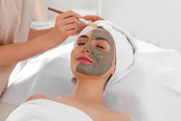 Kosmetolog Tillämpa Lera Mask Unga Kvinnans Ansikte Salong Närbild — Stockfoto