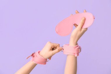 Pembe kelepçeli ve maskeli bir kadın seks dükkanından leylak arka planda.