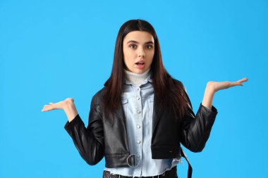 Mavi arka planda deri ceketli kafası karışmış genç bir kadın.