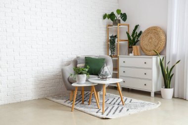 Hafif oturma odasındaki masaların üzerinde minderleri ve çiçekleri olan rahat gri koltuklar.