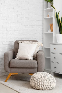 Aydınlık oturma odasının iç tarafında yastıkları olan rahat gri bir koltuk.