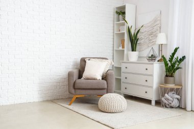 Aydınlık oturma odasının iç tarafında yastıkları olan rahat gri bir koltuk.