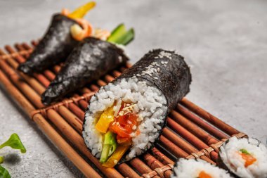 Lezzetli suşi rulosu olan bambu hasırı ve grunge arkaplanda koni, yakın plan.